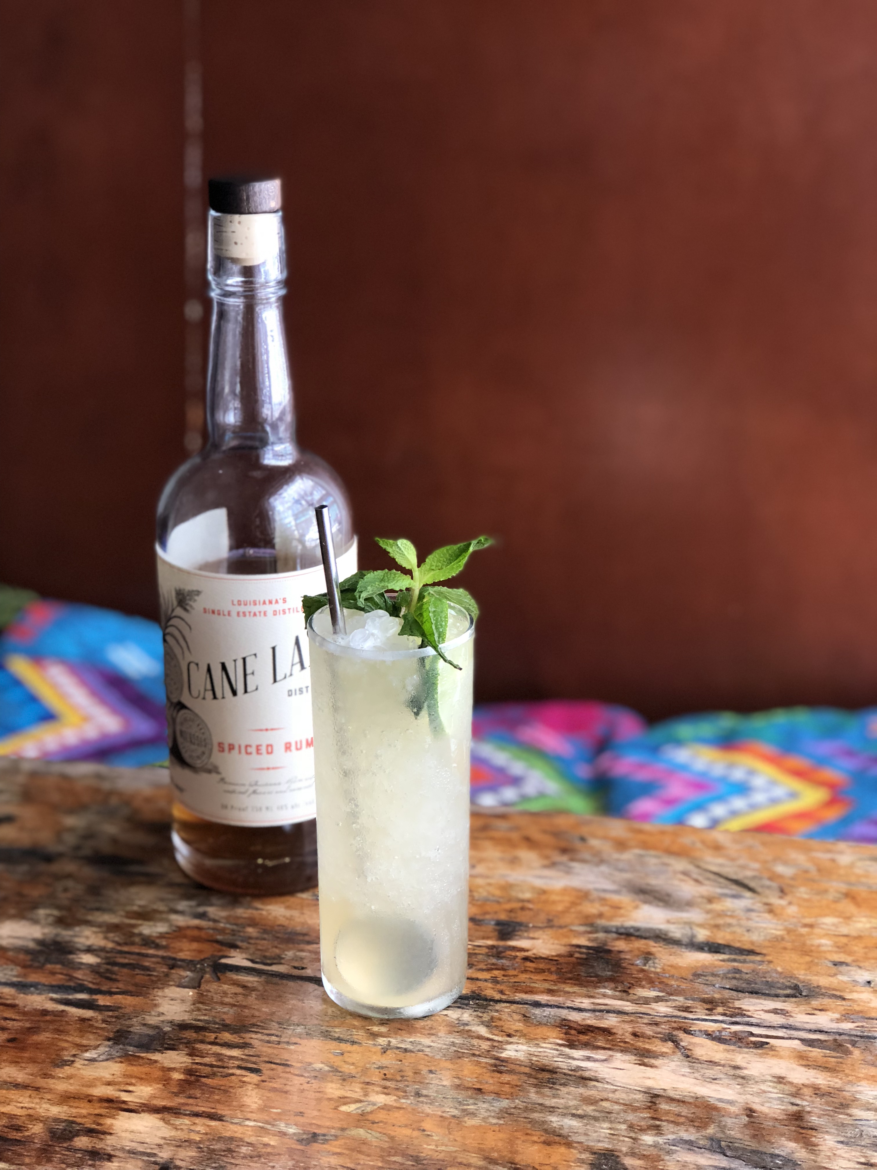 a drink with a sprig of herbs in a glass on a table next to a bottle